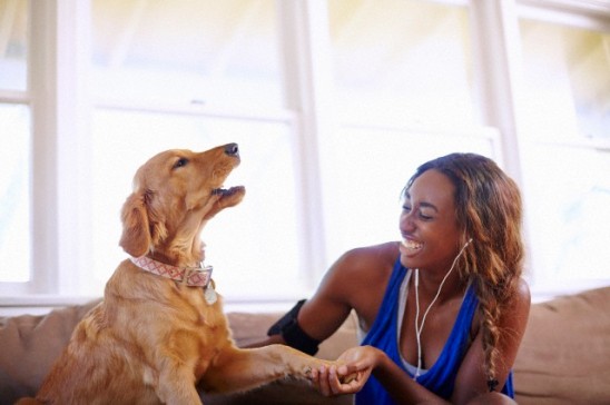 27 Jun 2014 --- Young woman taking a training break, petting dog in sitting room --- Image by © Kevin Kozicki/Image Source/Corbis
